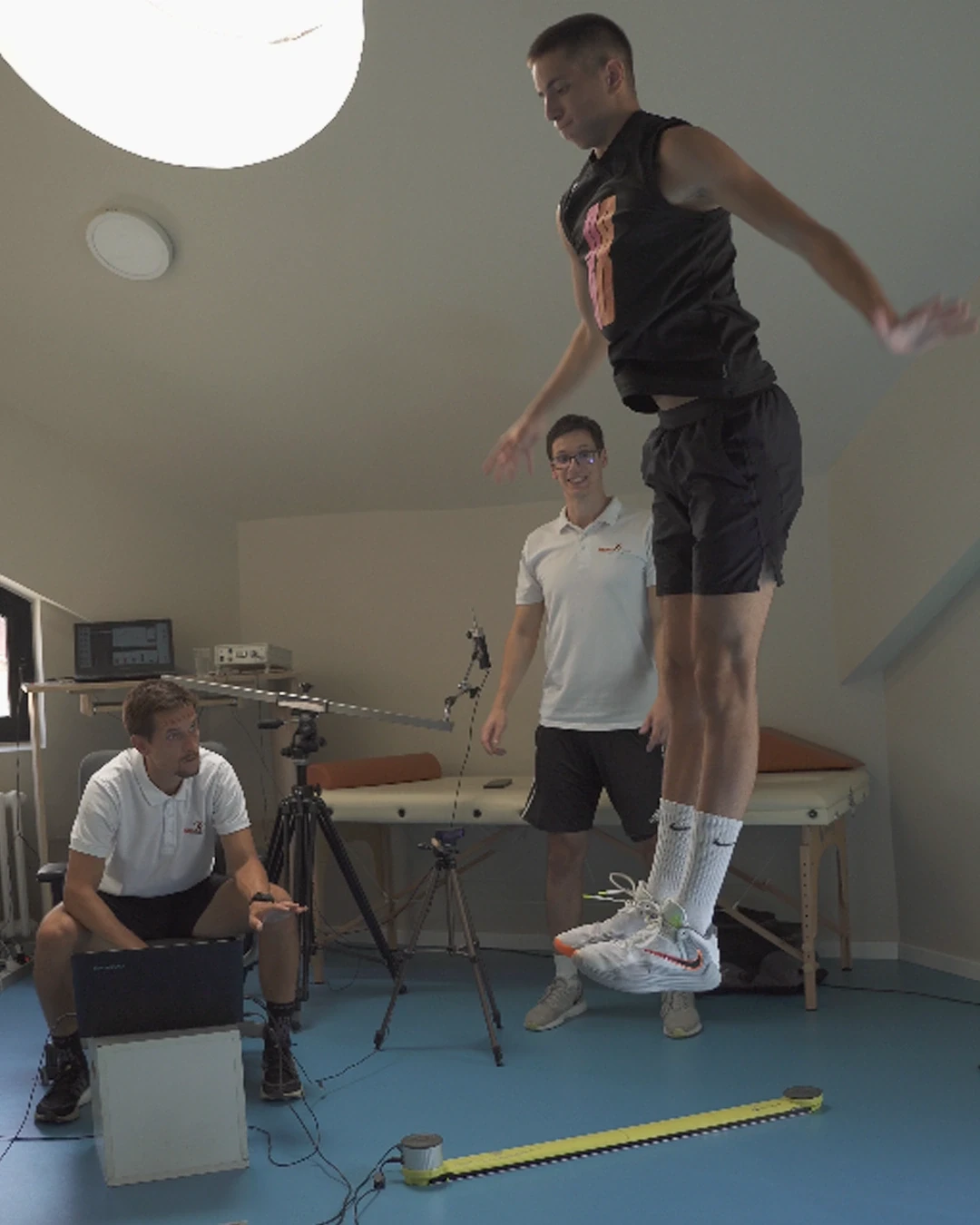 Merenje skoka na Optojump sistemu — sportista u odrazu iznad optičkih letvica, dva trenera prate seriju skokova.
